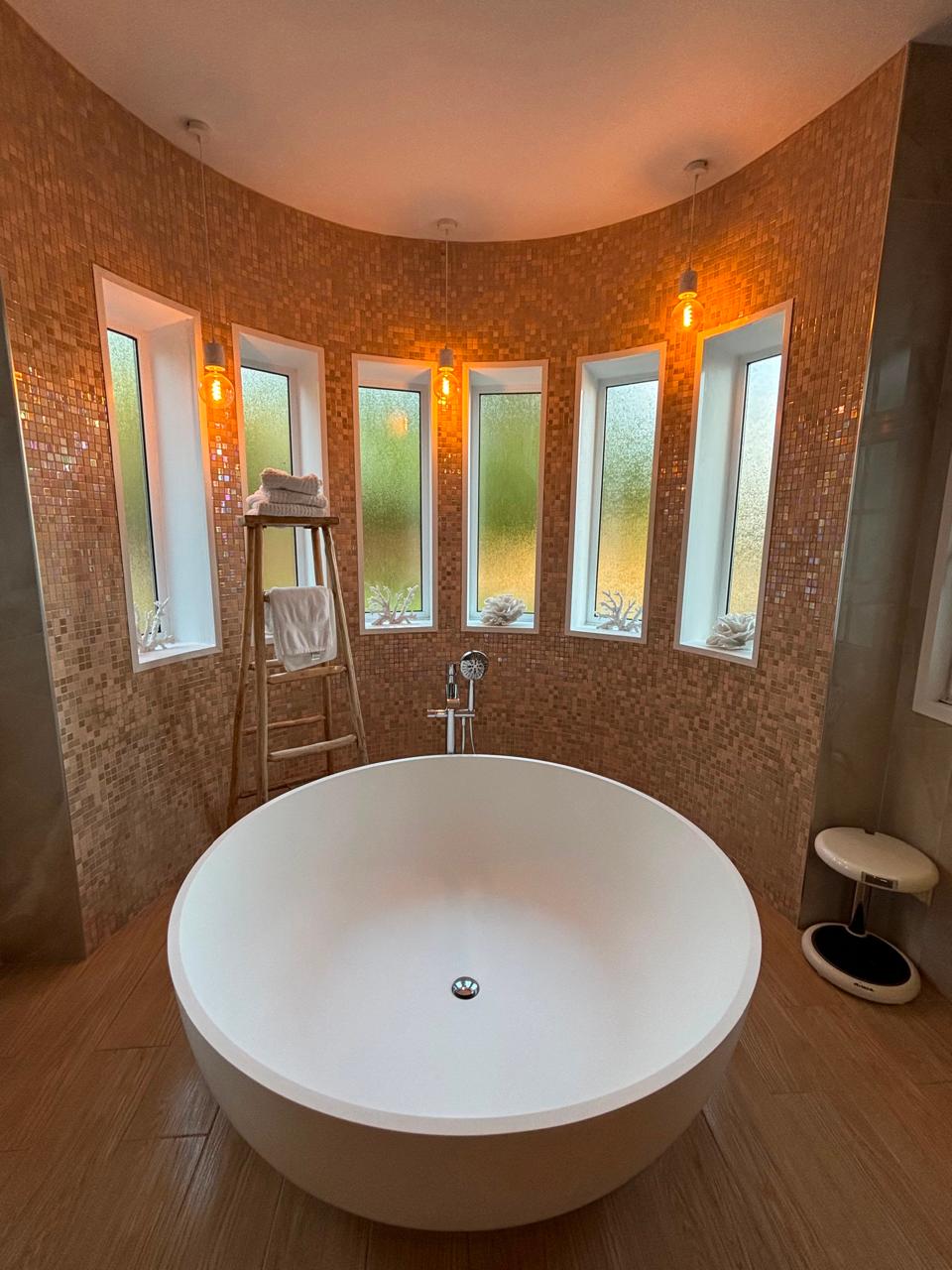 Remodeled bathroom with freestanding soaking tub and detailed mosaic tile walls
